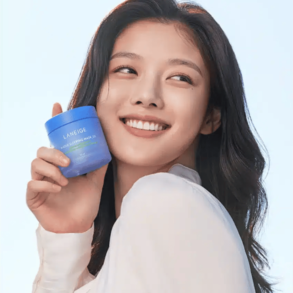 Smilende kvinde holder en blå krukke af LANEIGE Water Sleeping Mask foran lyseblå baggrund.