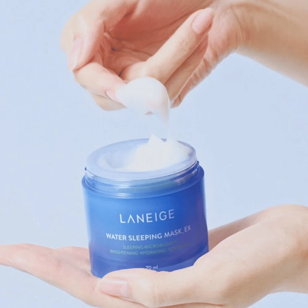 En hånd skovler op LANEIGE Water Sleeping Mask fra en blå krukke, med fokus på den gelélignende konsistens mod lyseblå baggrund.