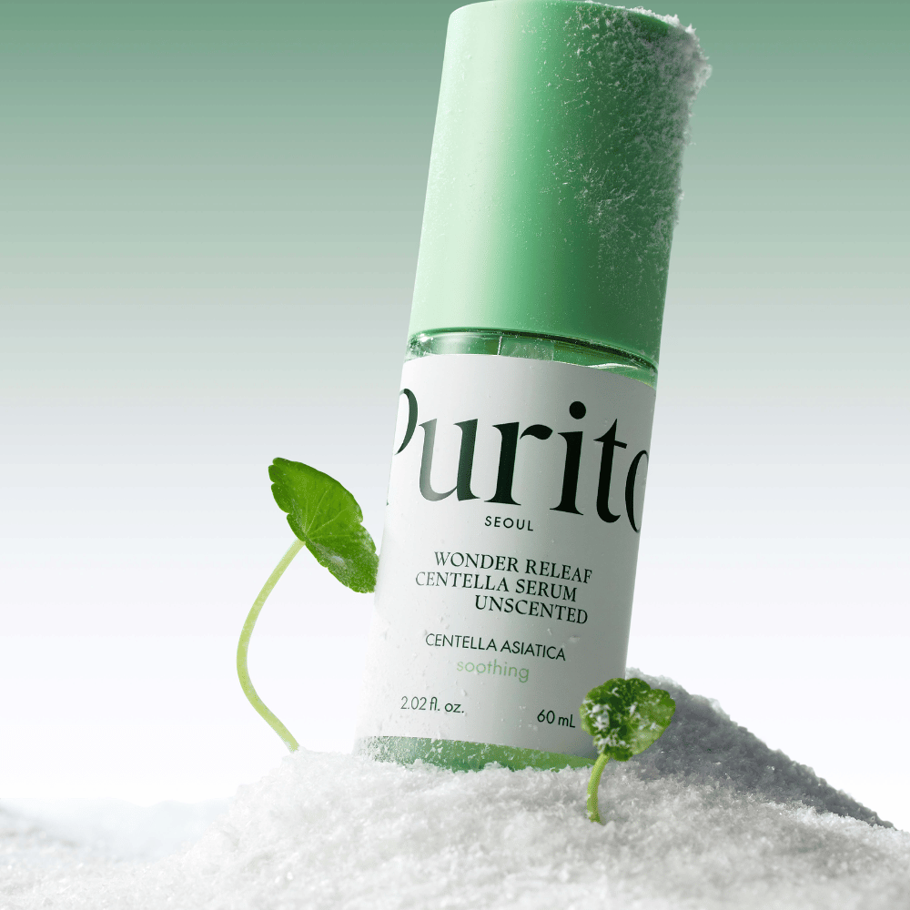 Flaske med Purito Centella Serum ligger i sne, grønne blade ses, mod en blød grøn baggrund.
