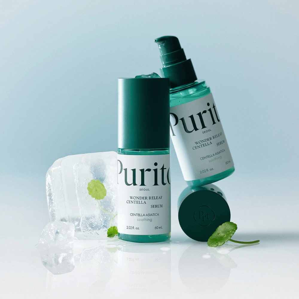 To flasker af Purito Wonder Releaf Centella Serum, en stående og en liggende, omgivet af isterninger med centellablade indeni samt et løst blad på en lyseblå overflade.