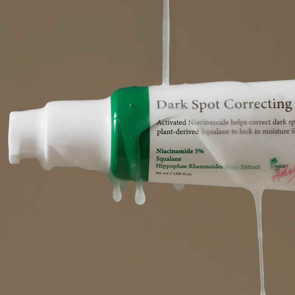 Nærbillede af en pumpeflaske af Axis-Y Dark Spot Correcting Glow Serum med hvid emballage og grøn hætte, dækket af løbende gennemsigtig væske.