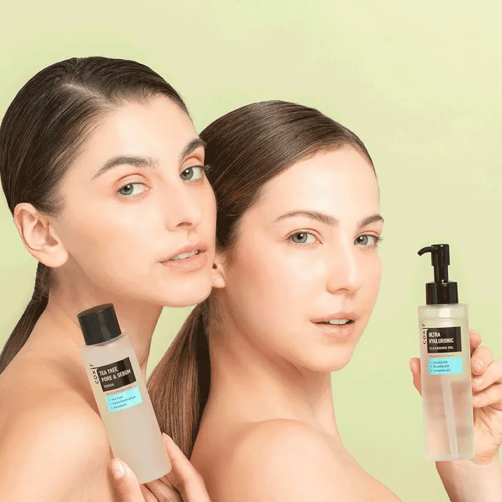 To kvinder med bare skuldre poserer med hudplejeprodukter; den ene holder en flaske mærket "TEA TREE PORE & SEBUM", og den anden en pumpeflaske mærket "ULTRA HYALURONIC CLEANSING OIL". De står foran en lysegrøn baggrund.