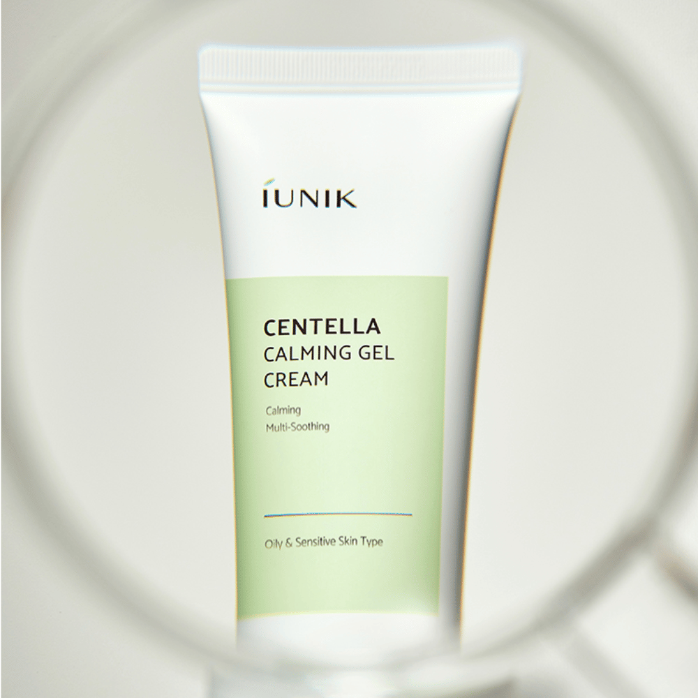 Et rør iUNIK Centella Calming Gel Cream med hvid og lysegrøn design står oprejst, set gennem en rund forstørrelsesglaslignende ramme.