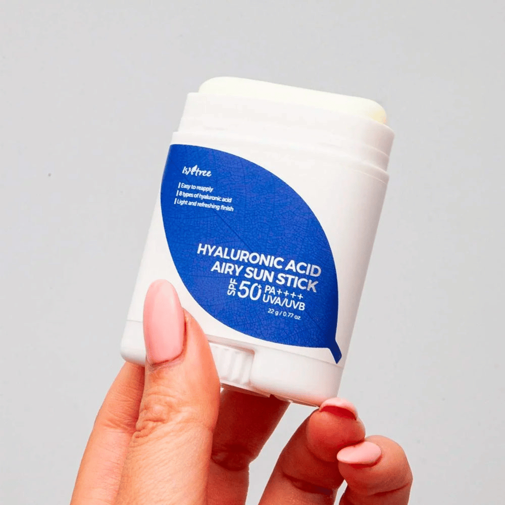 En hånd holder i en hvid solstick med blå etiket fra mærket Isntree. Produktet hedder "Hyaluronic Acid Airy Sun Stick" og har solbeskyttelsesfaktor SPF 50+ PA++++.