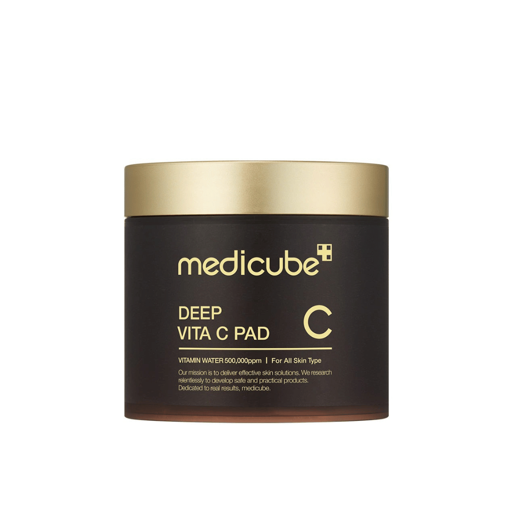En krukke fra medicube, mærket "Deep Vita C Pad", med guldlåg og mørk krop. Tekst på krukken angiver C-vitamin og egnethed for alle hudtyper. Baggrunden er neutral.