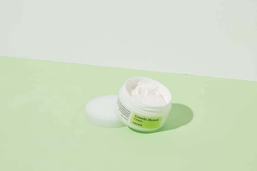En krukke COSRX Centella Blemish Cream 30ml som står på en grøn overflade.
