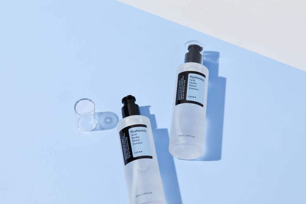 COSRX:s Hyaluronic Acid Hydra Power Essence 100ml giver fugtgivende fordele på blå overflade.