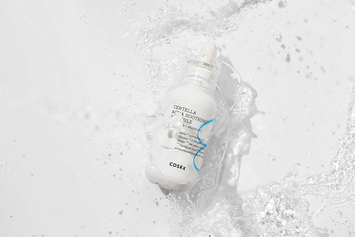 En flaske COSRX Centella Aqua Soothing Ampoule 40ml som sprøjter på en hvid overflade, reducerer rødme og giver beroligende fugt.
