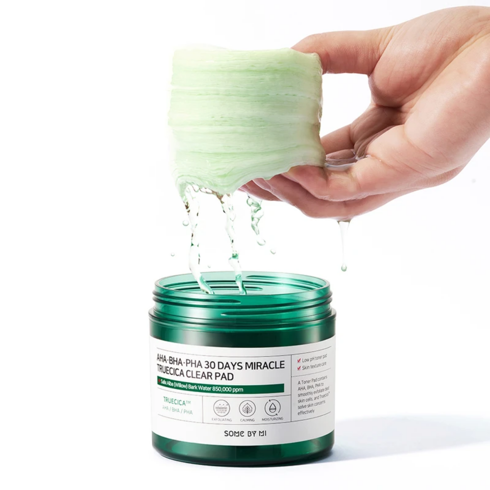 En hånd hælder en grøn væske i en krukke til SOME BY MI:s AHA, BHA, PHA 30 Days Miracle Truecica Clear Pad 70 stk akneudbrud behandling.