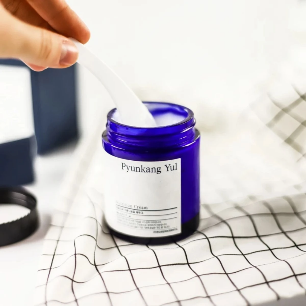 En person bruger en dåse Pyunkang Yul Nutrition Cream 100ml på et bord.