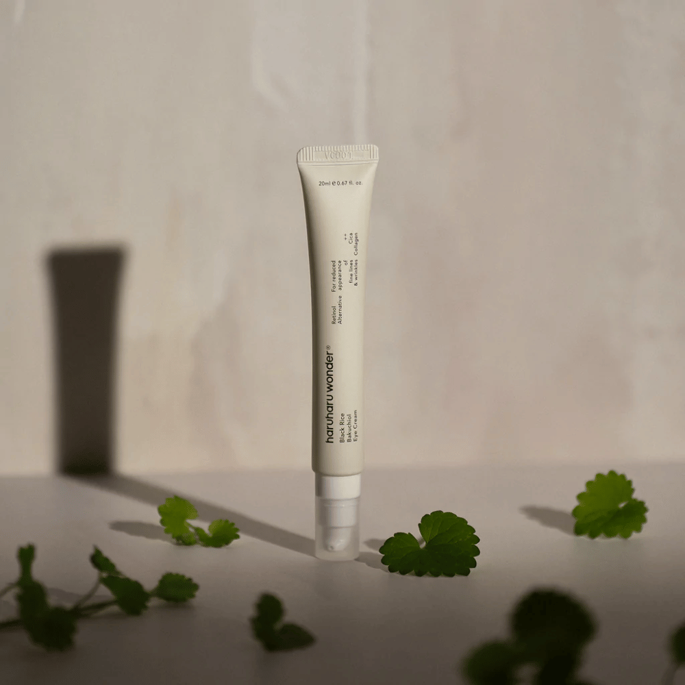 En tube Haruharu Wonder Black Rice Bakuchiol Eye Cream 20ml omgivet af grønne blade, fokuseret på synligheden af rynker og fine linjer.