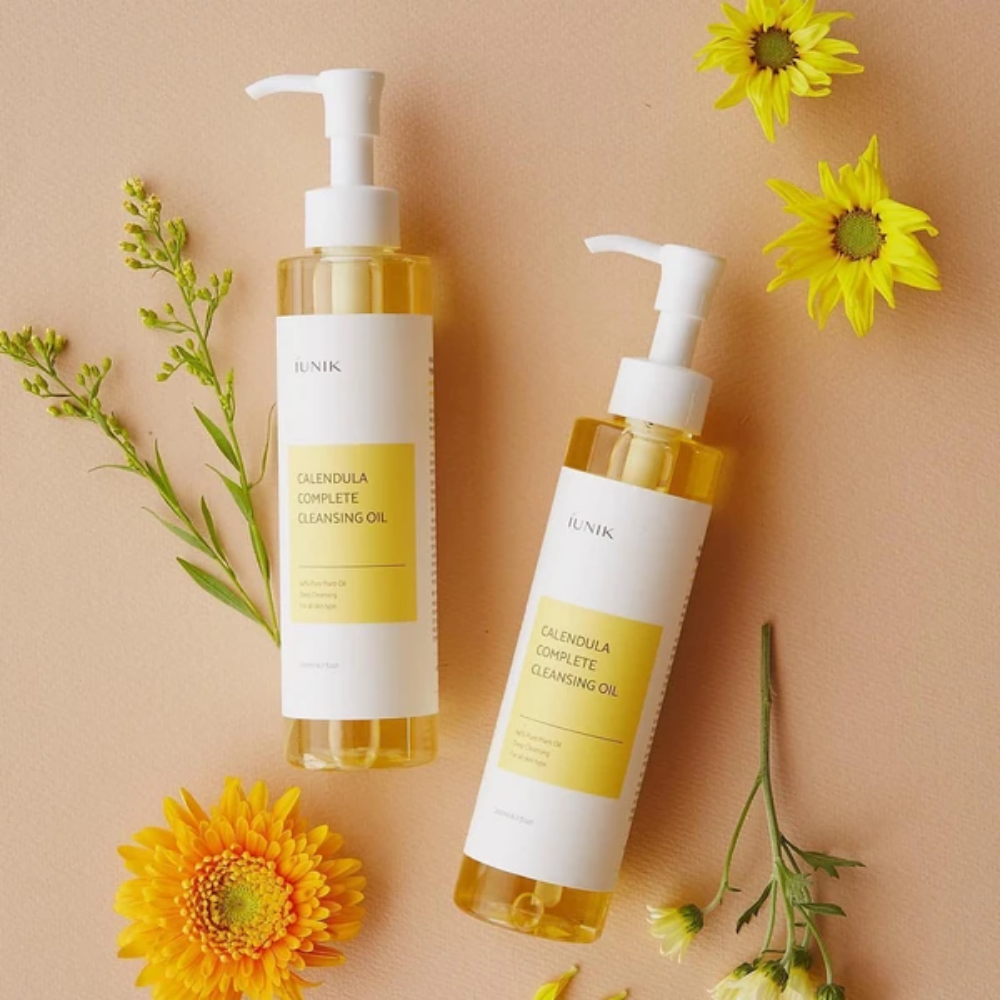 To flasker iUNIK Calendula Complete Cleansing Oil 200ml med gule blomster på beige baggrund, infunderet med planteolie.