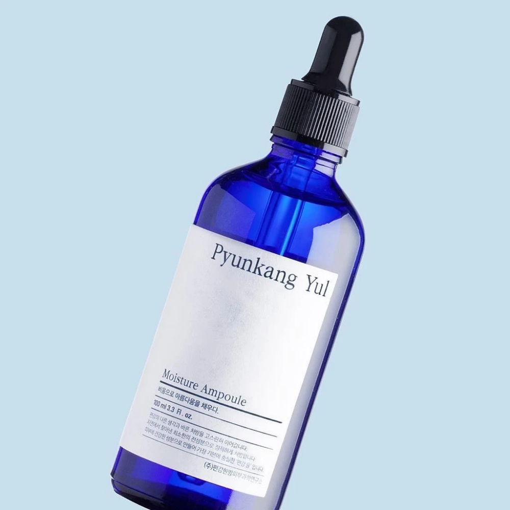 En blå flaske på blå baggrund med Pyunkang Yul's Moisture Ampoule 100ml serum.