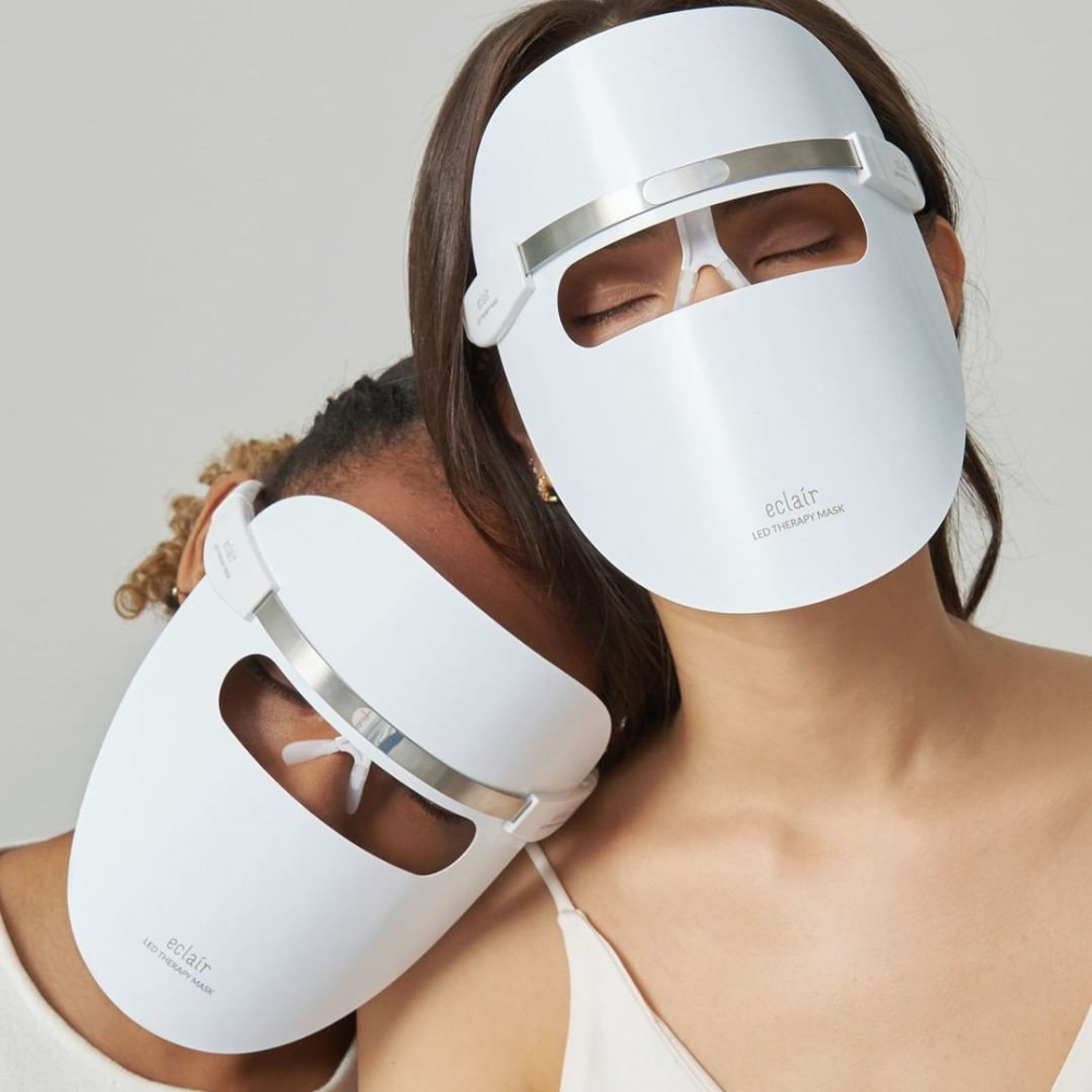 To kvinder, der bærer hvide masker, demonstrerer ECLAIR LED Therapy Mask for hudtoneforbedringer.