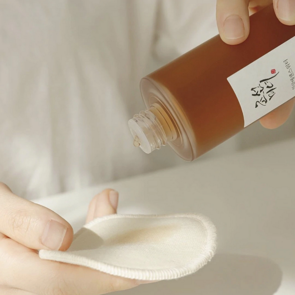 En person der hælder Beauty of Joseon Ginseng Essence Water 150ml på en klud for at tackle tør hud og reducere talgproduktion.