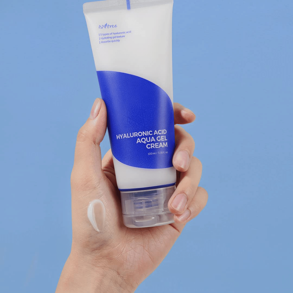 En hånd der holder et rør Isntree Hyaluronic Acid Aqua Gel Cream 100ml på en blå baggrund.